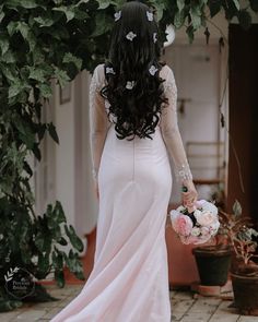 the back of a woman in a long pink dress with flowers on her head and arms