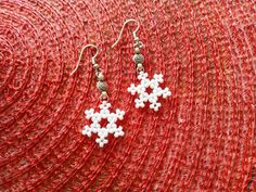 two white snowflakes are hanging from silver earwires on a red background