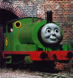 a thomas the tank engine is smiling in front of a brick wall