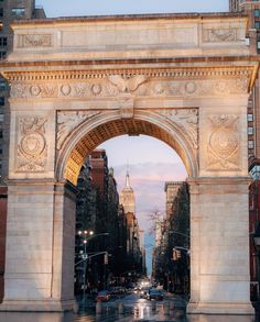 an arch in the middle of a city street with traffic going underneath it at dusk