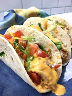 two tacos are sitting on top of a blue plate with yellow sauce and tomatoes