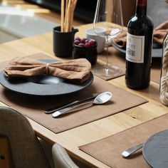 a wooden table topped with plates and silverware next to a bottle of red wine