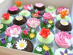 a box filled with lots of cupcakes covered in frosting and colorful flowers