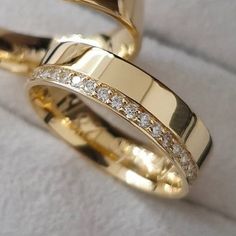 two gold wedding rings sitting on top of each other with diamonds in the middle and sides