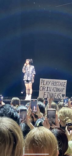 a woman standing on top of a stage surrounded by people holding up cell phones in front of her