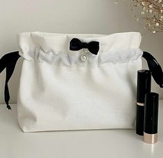 a white bag with a black bow tie next to two lipstick tubes on a table