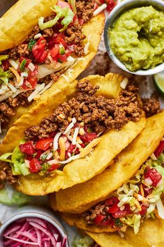 three tacos with toppings and guacamole in bowls on the side