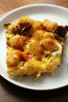 a white plate topped with an omelet covered in meat and cheese on top of a wooden table