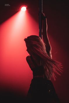 a woman with long hair standing on a pole in front of a red light and spotlight