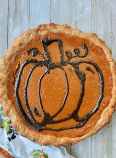 a pumpkin pie with chocolate icing on top sitting on a table next to a napkin