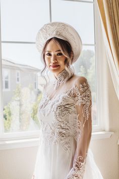 a woman in a white dress and hat standing by a window with her hands on her hips