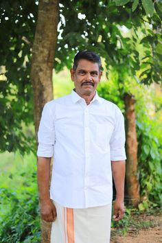 a man standing in front of a tree with his hands on his hips and looking at the camera