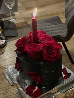 a black cake with red roses and a single candle on top is sitting on a table