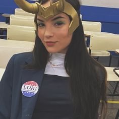 a woman with long hair wearing a costume and helmet on her head, standing in front of rows of chairs