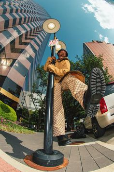 a woman standing on top of a lamp post next to a white car in front of a building