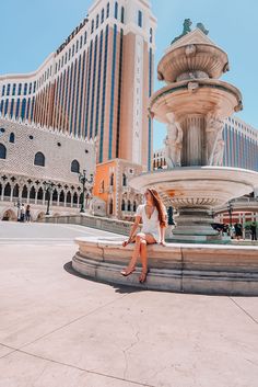 a woman sitting on the edge of a fountain in front of a hotel and casino