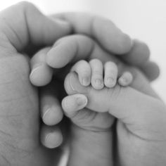 a black and white photo of a baby's hand holding its mother's finger