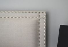 an upholstered headboard with beading on the sides and a black lamp next to it