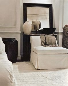 a white chair sitting in front of a mirror on top of a dresser next to a vase