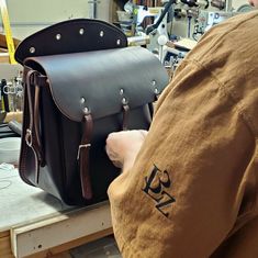 a man holding a brown leather bag in his hand and working on it's side