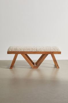 a wooden bench sitting on top of a floor next to a white wall and cement floor