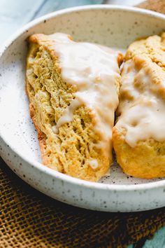 two scones with icing in a white bowl on a blue and brown cloth