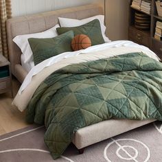 a bed with green and white comforter, pillows and a basketball on the pillow