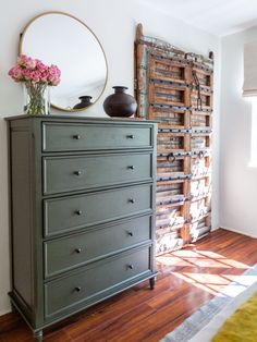 a green dresser with flowers on top in front of a mirror and wooden shutters