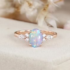 a white opal and diamond ring sitting on top of a piece of cloth with flowers in the background