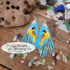 two blue and yellow bird beaded earrings sitting on top of a wooden table