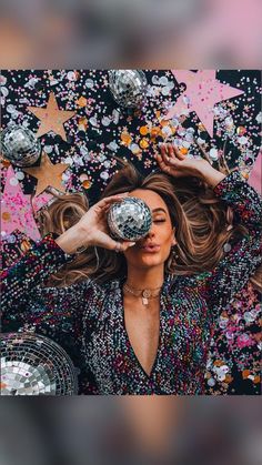 a woman holding a disco ball in front of her face surrounded by confetti and stars