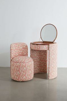 an upholstered vanity and stool with a round mirror on the top, in front of a white wall