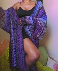 a woman wearing a purple and blue crocheted shawl sitting on top of a bed