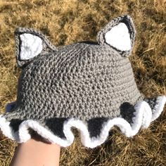 a hand is holding a crocheted gray hat with white ruffles on it