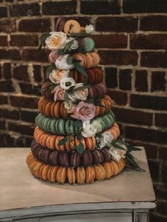 a stack of macaroons is decorated with flowers and leaves on a table in front of a brick wall