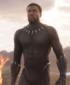 black panther standing in front of fire with his hands on his hips and looking at the camera