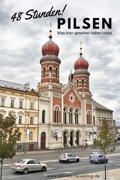 an old building with two red domes on it's roof and cars driving down the street