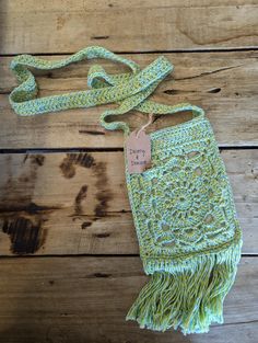 a green crocheted bag with a tag on it sitting on a wooden surface