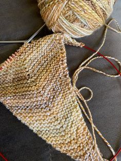 two skeins of yarn sitting on top of a piece of cloth next to some knitting needles