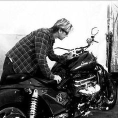 a man sitting on top of a motorcycle in front of a white wall and looking at it