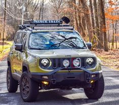 a green jeep is parked on the side of the road in front of some trees