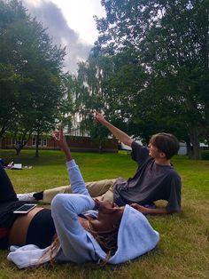 two people sitting on the grass with their arms in the air and one person pointing at something