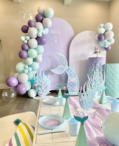 a table set up for a mermaid themed birthday party with balloons and paper fish decorations