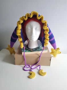 a white mannequin head wearing a purple and yellow knitted hat on top of a cardboard box