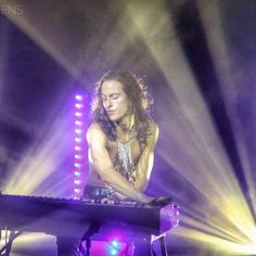 a man that is sitting at a keyboard in the middle of a stage with lights behind him