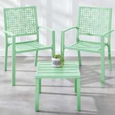 two green chairs and a small table in front of a white wall with a potted plant on it