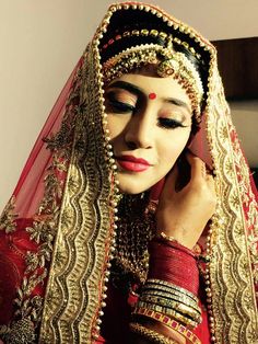 a woman in a red and gold bridal outfit with her hands on her head