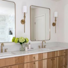 a bathroom with two sinks, mirrors and flowers in vases on the counter top