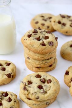 chocolate chip cookies next to a glass of milk on a marble counter top with a jar of milk in the background