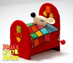 a small stuffed animal laying on top of a red bed with a colorful blanket and pillow